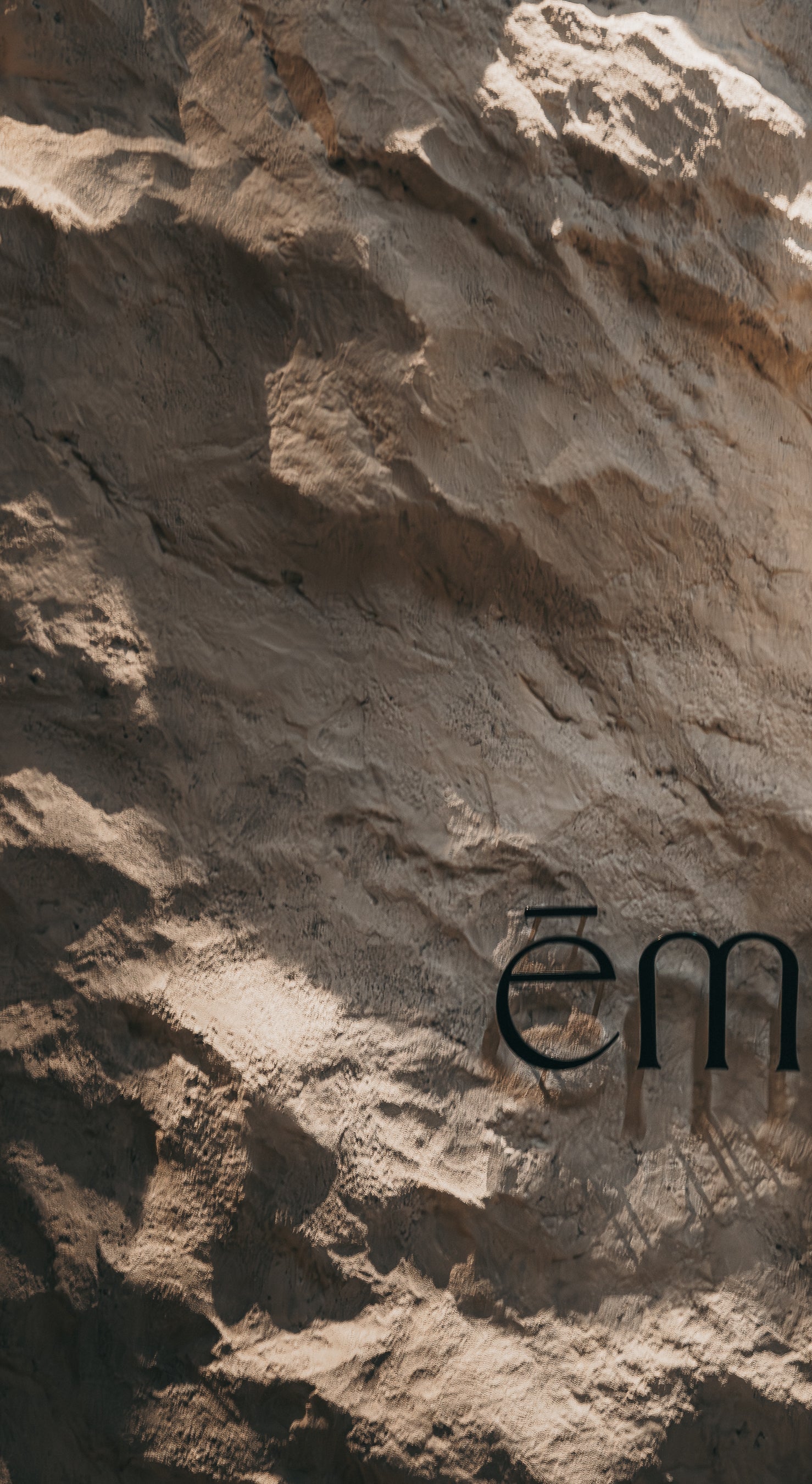 Text 'ēm' on a textured stone background